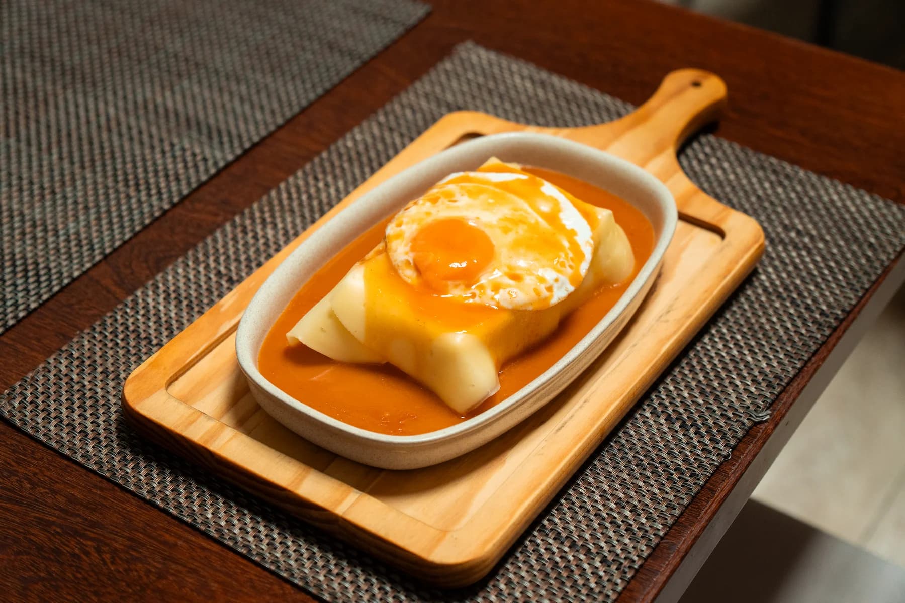 Francesinha com molho e ovo em tabuleiro de madeira